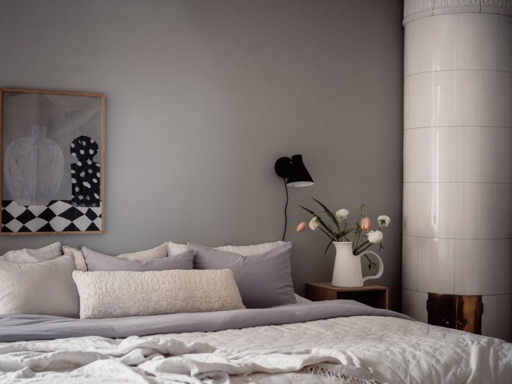 A bedroom with medium grey walls, art prints, white bedding, black wall lamps