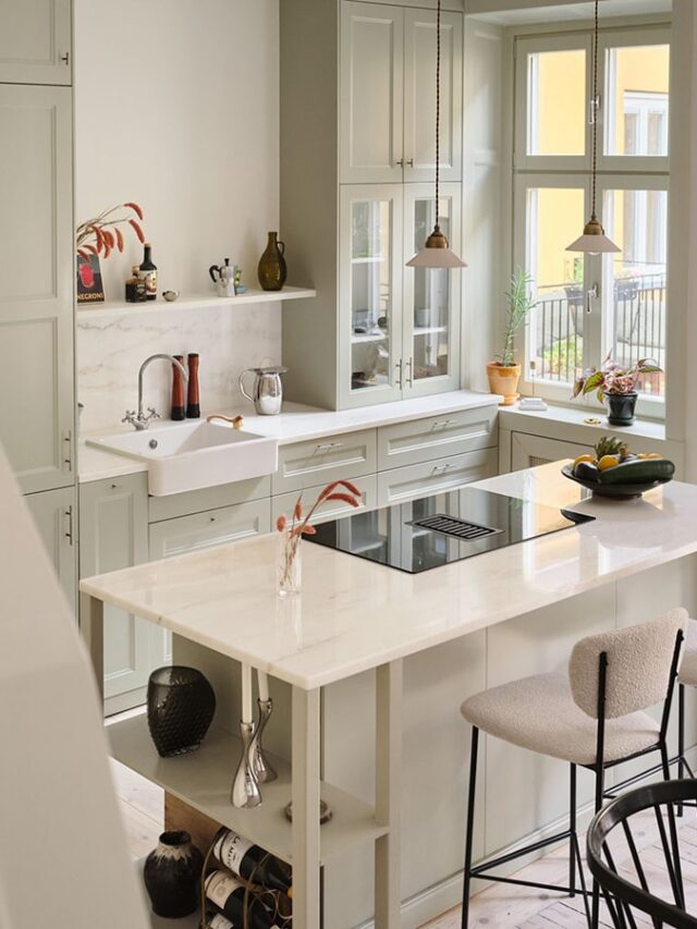A sage green kitchen with a white marble countertop, kitchen island and a farmhouse sink