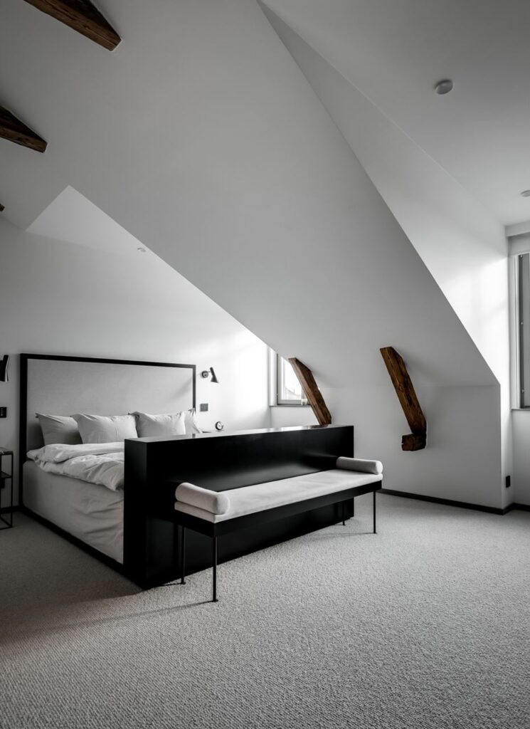 A spacious attic bedroom with crisp white walls and a black bed