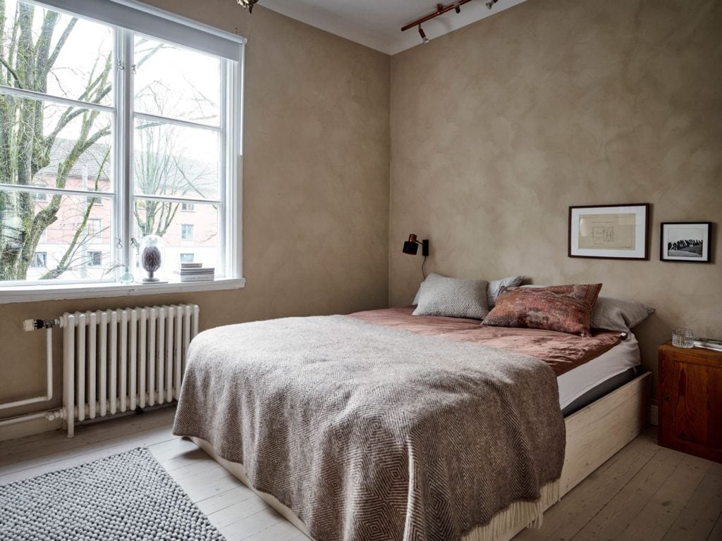 A bedroom with beige limewash walls and red and brown tones in the textiles