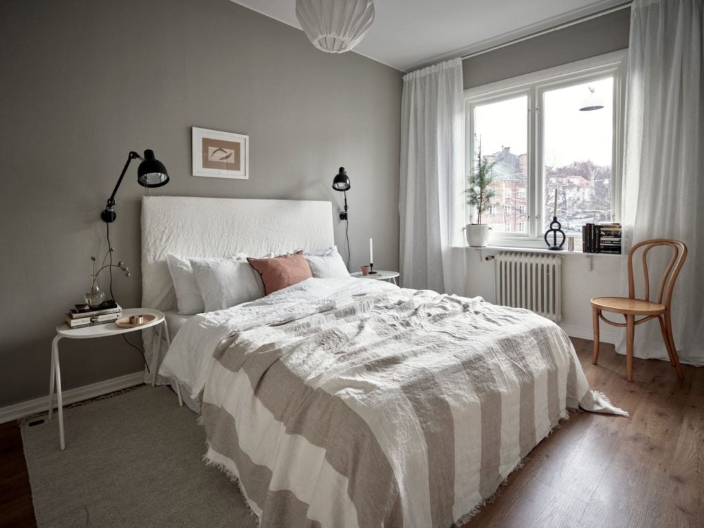 A medium grey wall color in a bedroom with a white linen bed frame, black wall lights and white bedside tables, striped blanket