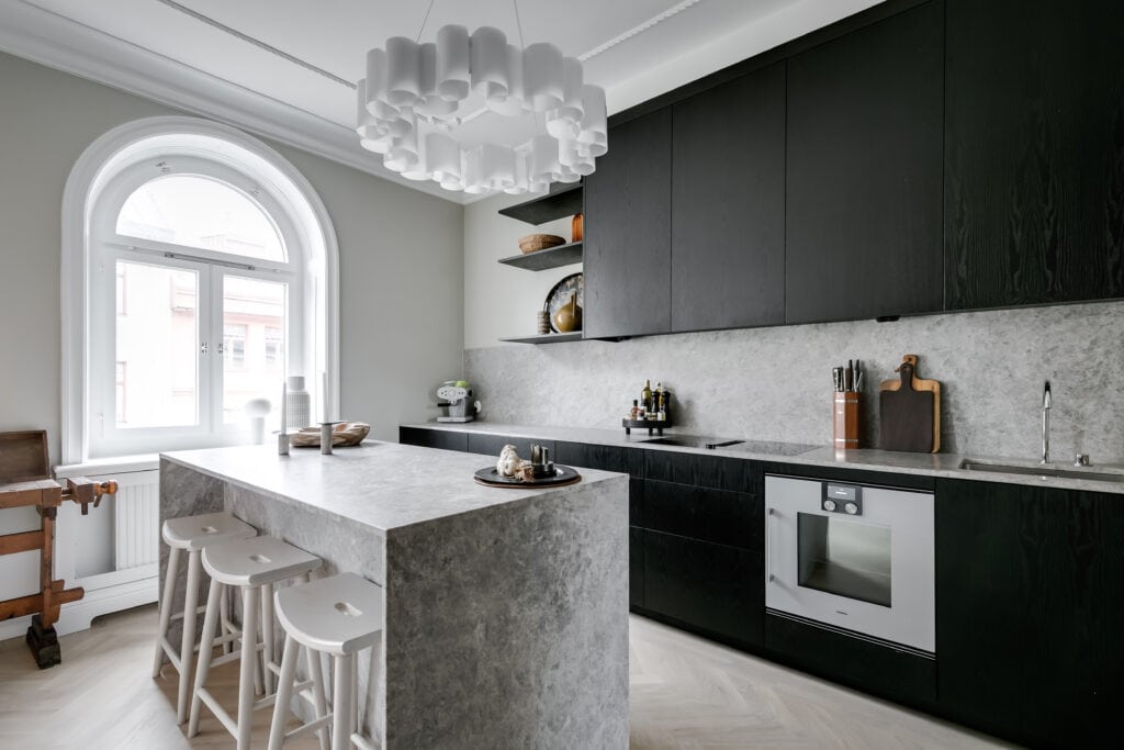 A grey marble kitchen island in a kitchen with black cabinets
