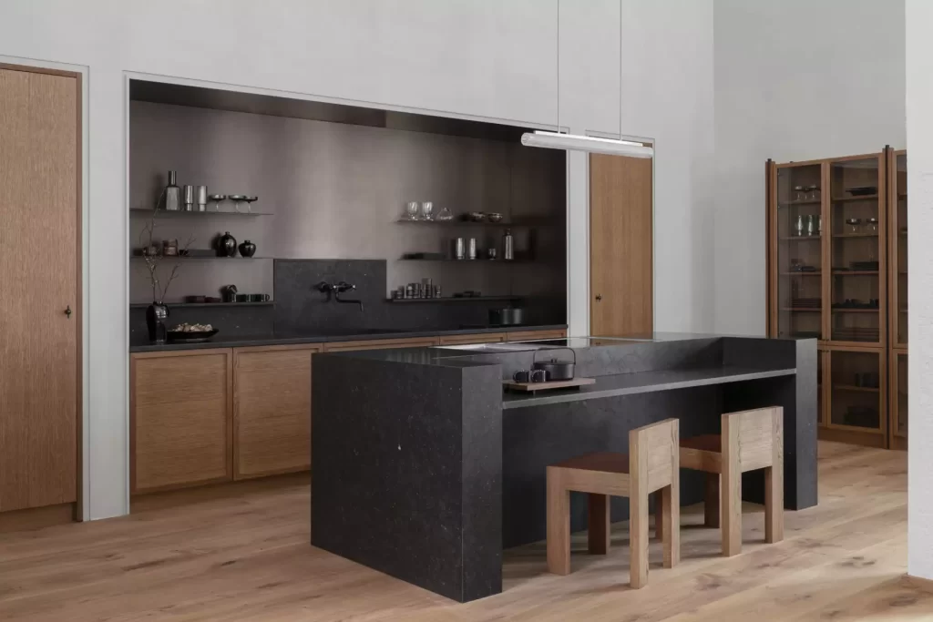 A black marble sculptural kitchen island with a seating area in a kitchen with wood cabinets
