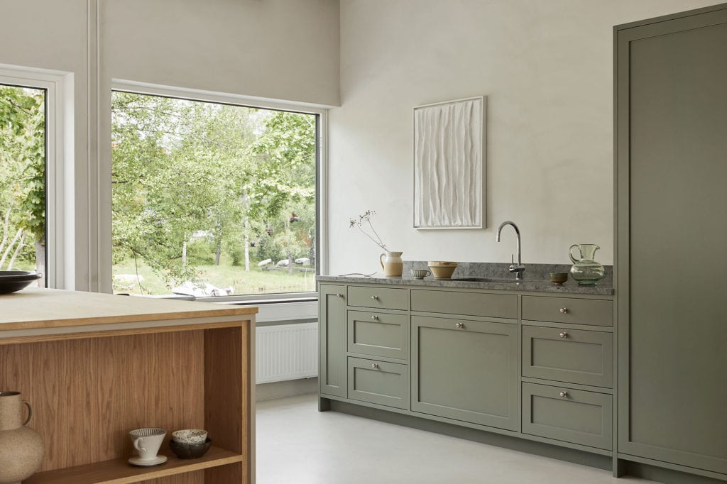 A minimal shaker kitchen with muted green kitchen cabinets and a grey stone countertop