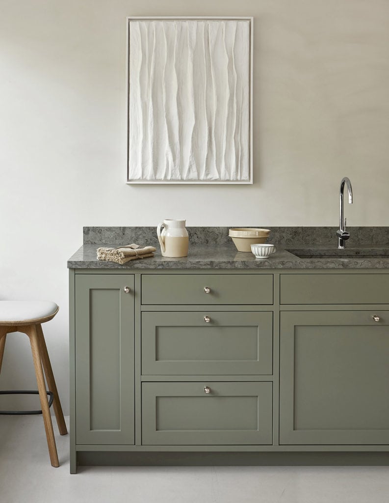 A minimal shaker kitchen with muted green kitchen cabinets and a grey stone countertop