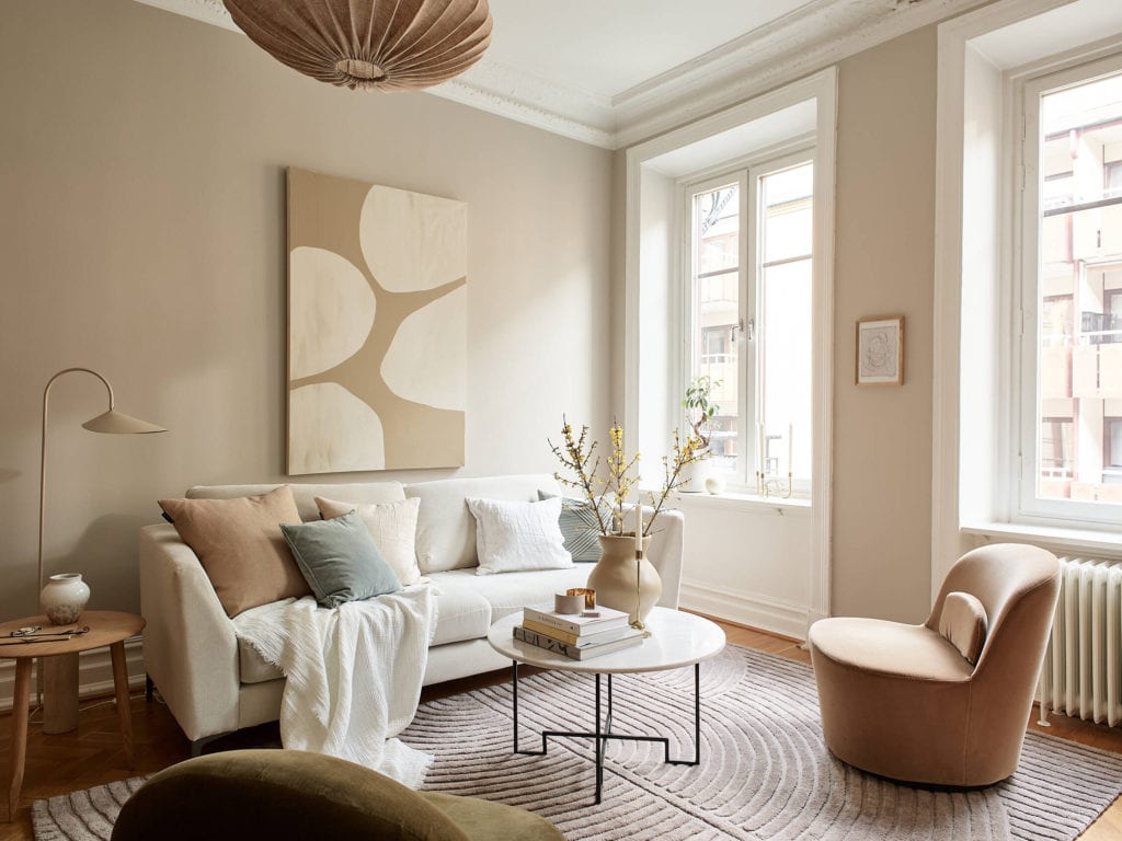 A living room with herringbone flooring and beige walls combined with fiurniture and soft furnishings in beige, white and natural wood tones