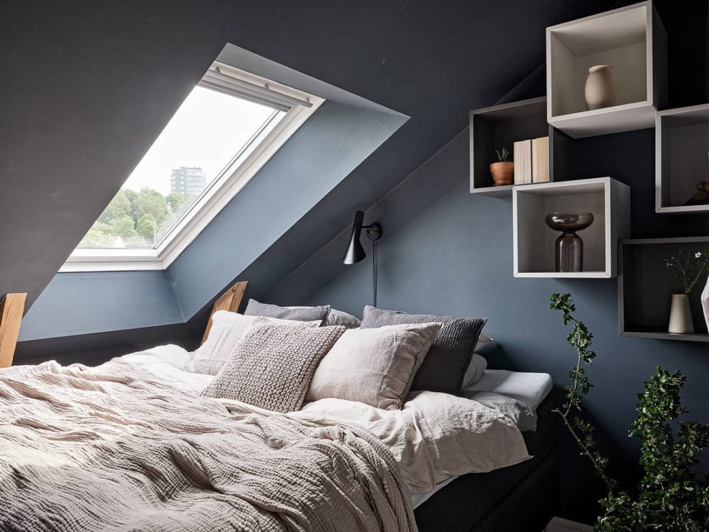 A tiny attic bedroom with a dusty blue wall color and a smart storage system on the wall