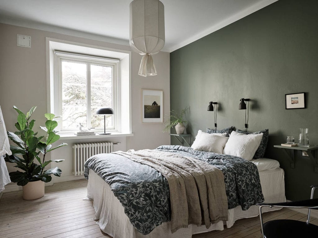 A bedroom with a dark green accent wall color