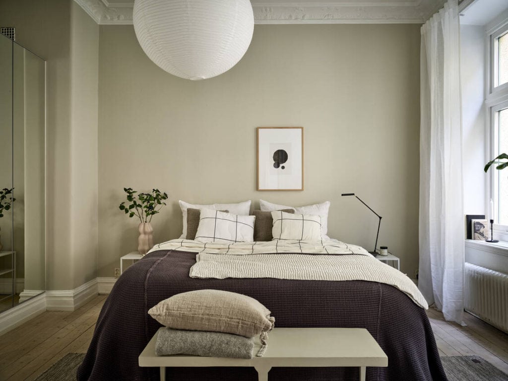 A bedroom with beige walls with green undertones and a mixture of black and white bedding on the bed