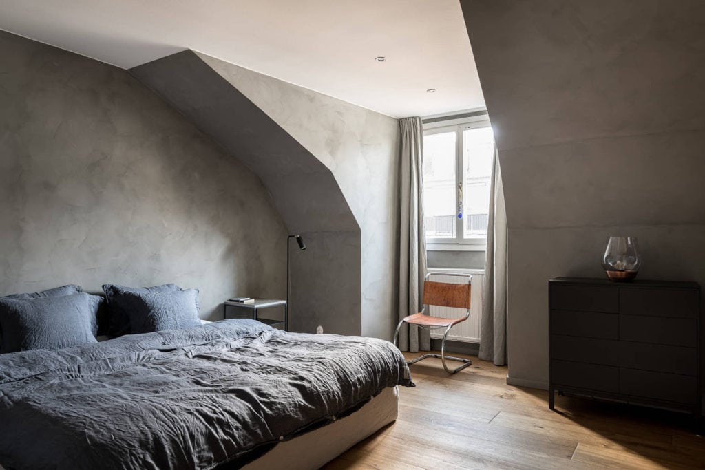 A attic bedroom with grey limewash paint ont he walls for a concrete look