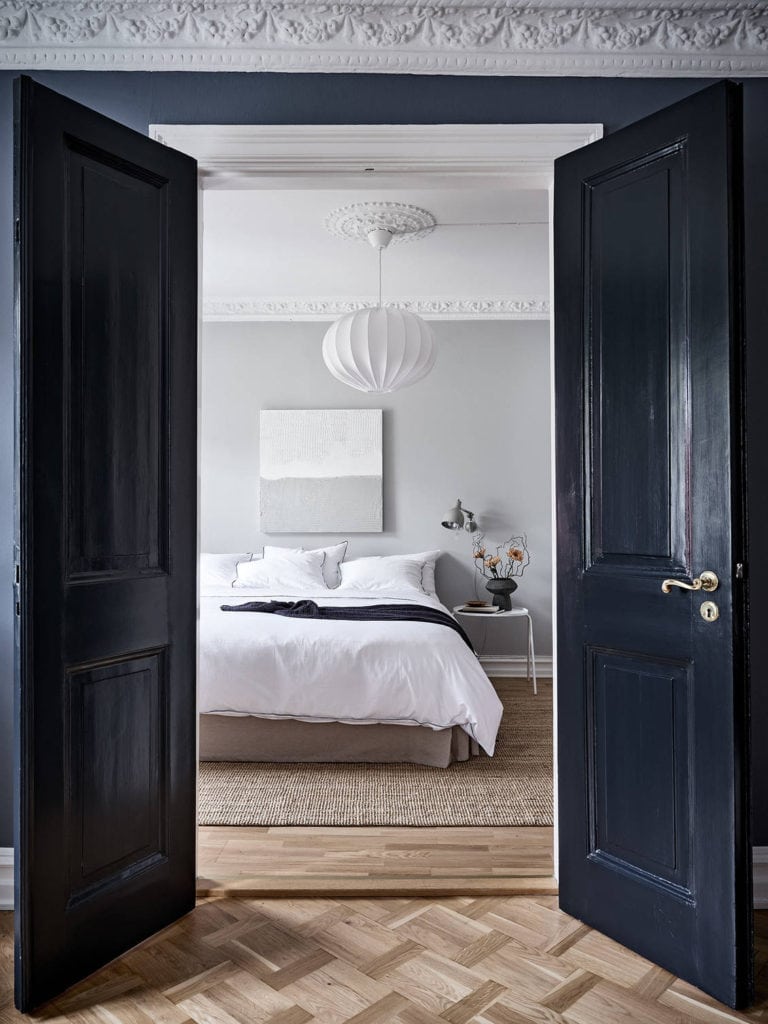 A light grey bedroom with blue doors, white bedding, grey wall lamps