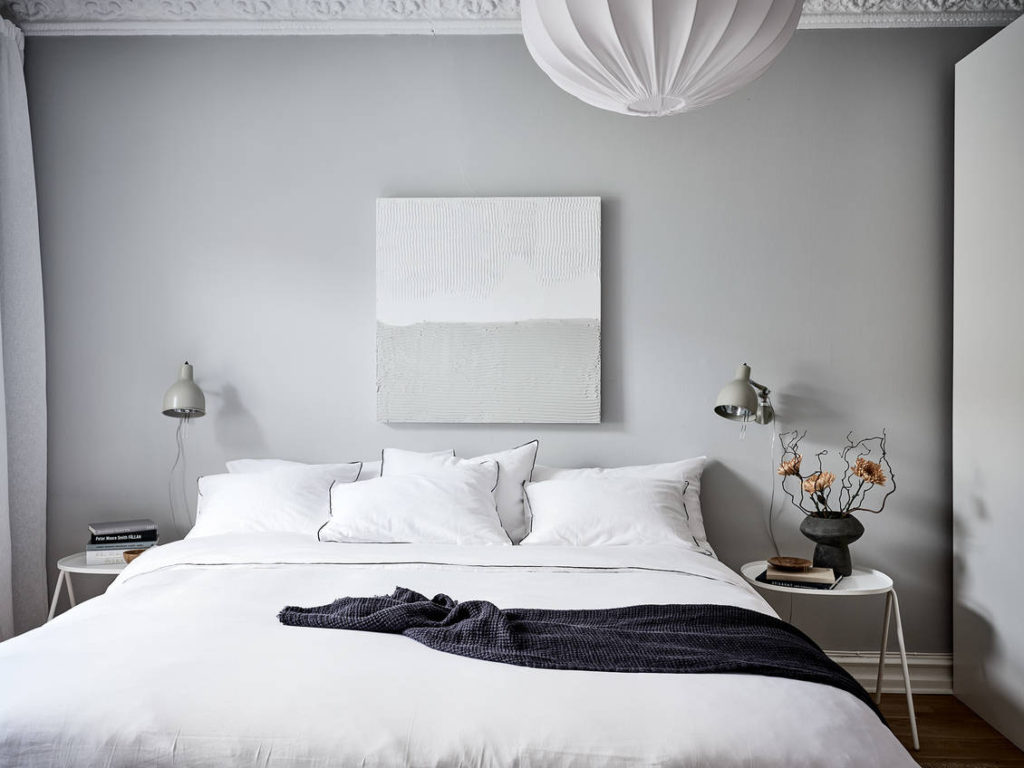 A light grey bedroom with blue doors, white bedding, grey wall lamps
